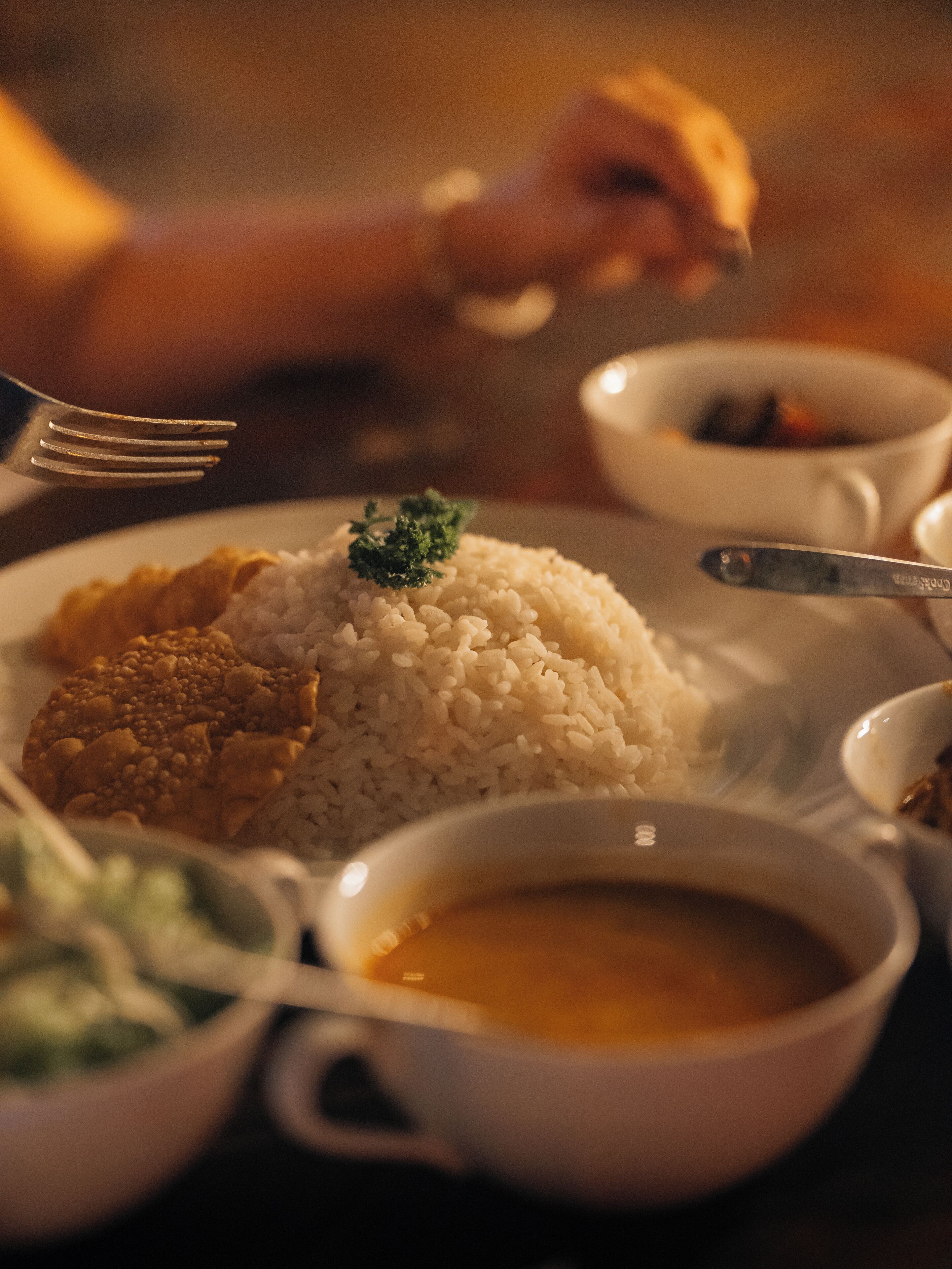 A dining table with a plate of rice, a bowl of soup, and a spoon.