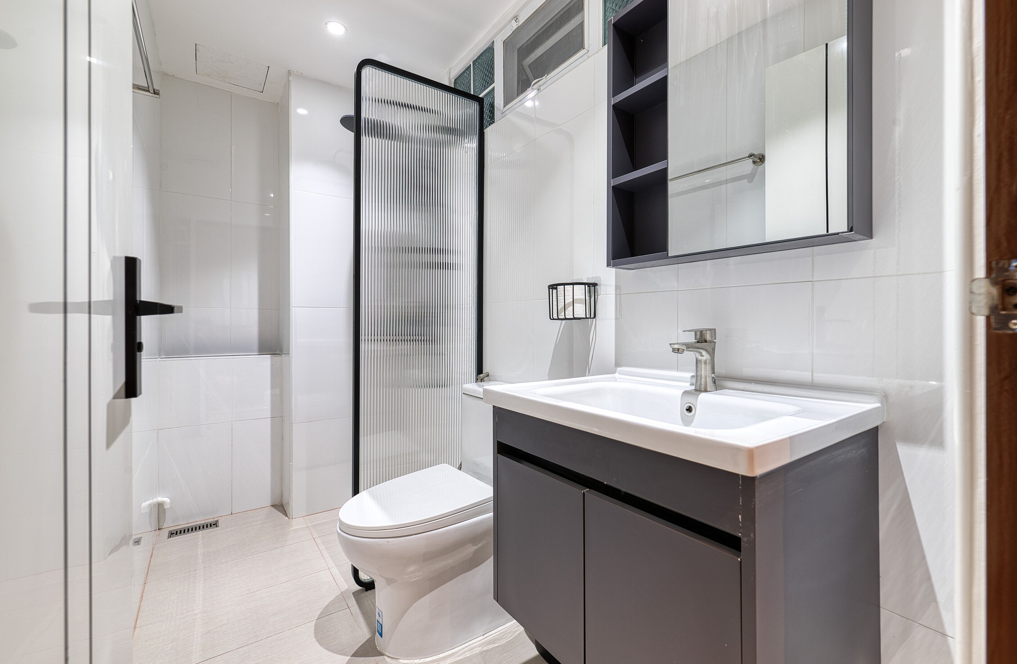 A modern bathroom with a glass shower enclosure, a white toilet, and a vanity with a sink and mirror.