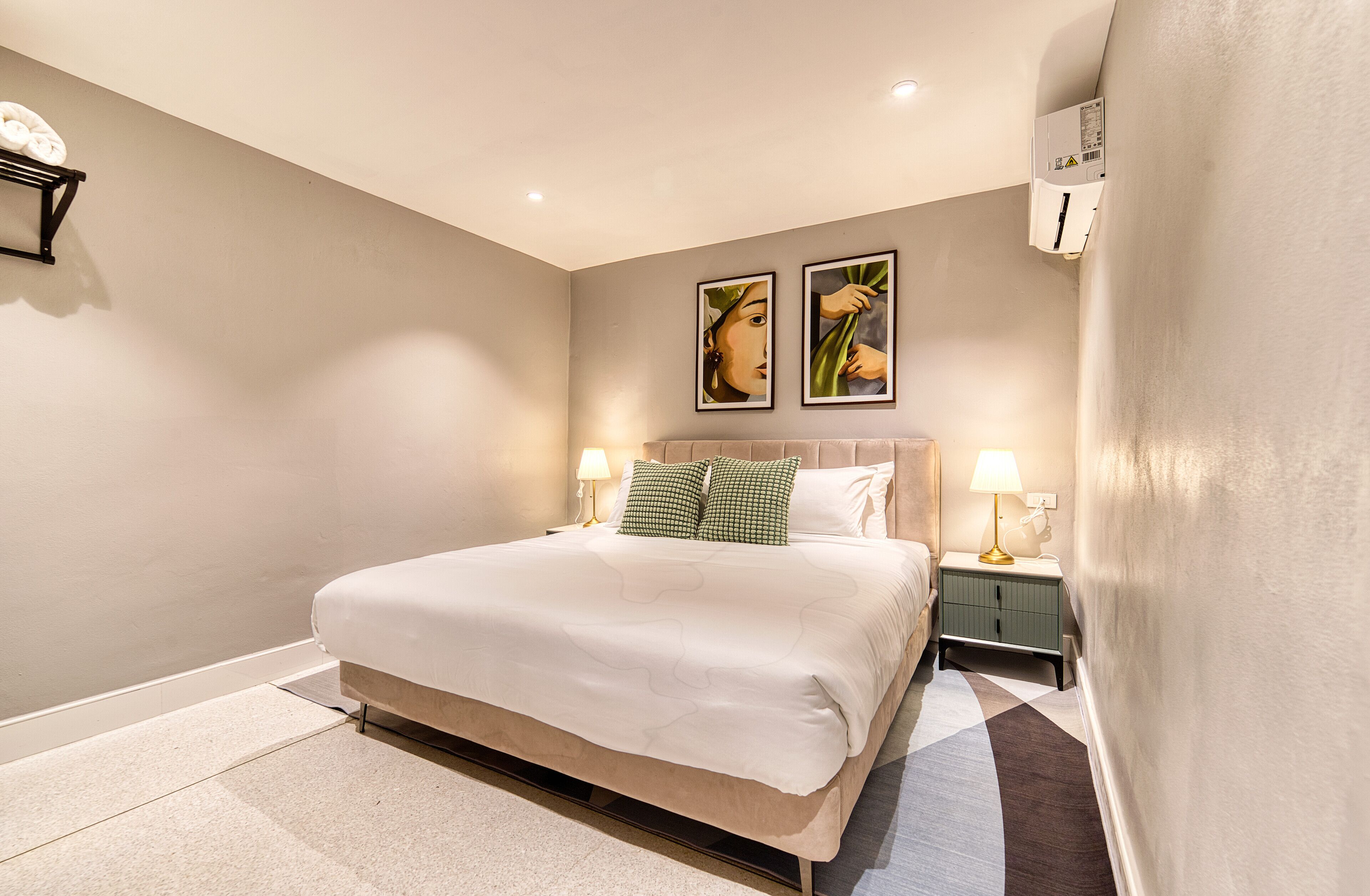 Une chambre à coucher avec un grand lit, deux lampes de chevet, une table de chevet et deux tableaux accrochés au mur.