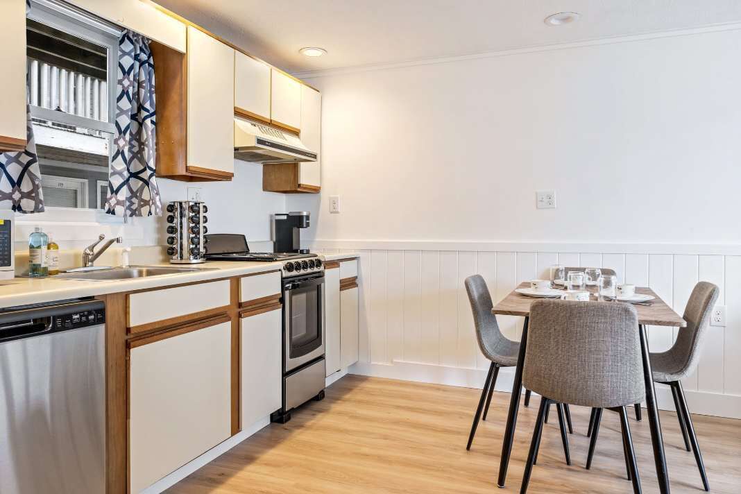 A compact kitchen with a dishwasher, stove, and dining area with chairs.
