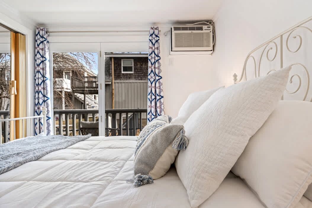 A bedroom with a bed, white bedding, and a balcony with patterned curtains.