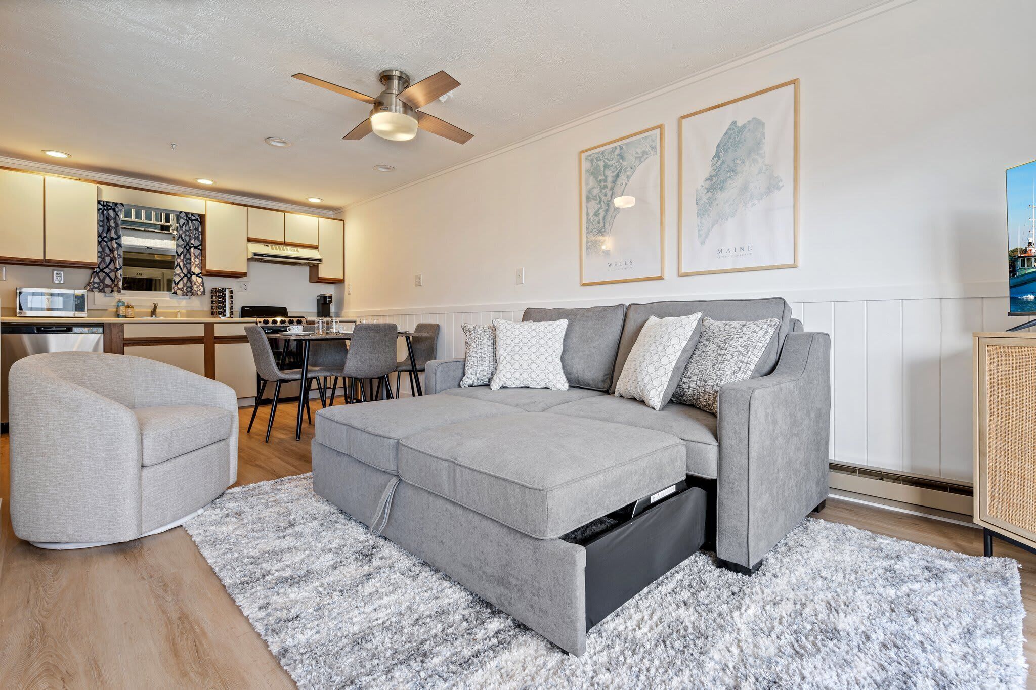 A modern living room with a grey sectional sofa, a grey armchair, and a dining area with a table and chairs.