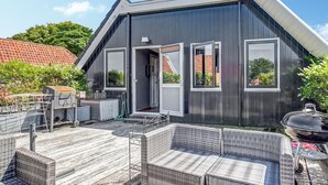A modern house with a dark exterior, large windows, and a covered patio with wicker furniture.