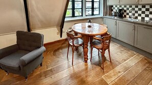 A dining area with a round wooden table and four chairs, a small gray armchair, and a window with curtains.