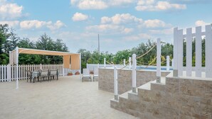 Un patio al aire libre con zona de estar cubierta, muros de piedra y cerca blanca.