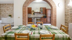 Un comedor con mantel a cuadros, sillas de madera y un arco de ladrillo que conduce a una cocina con armarios de madera y una estufa.