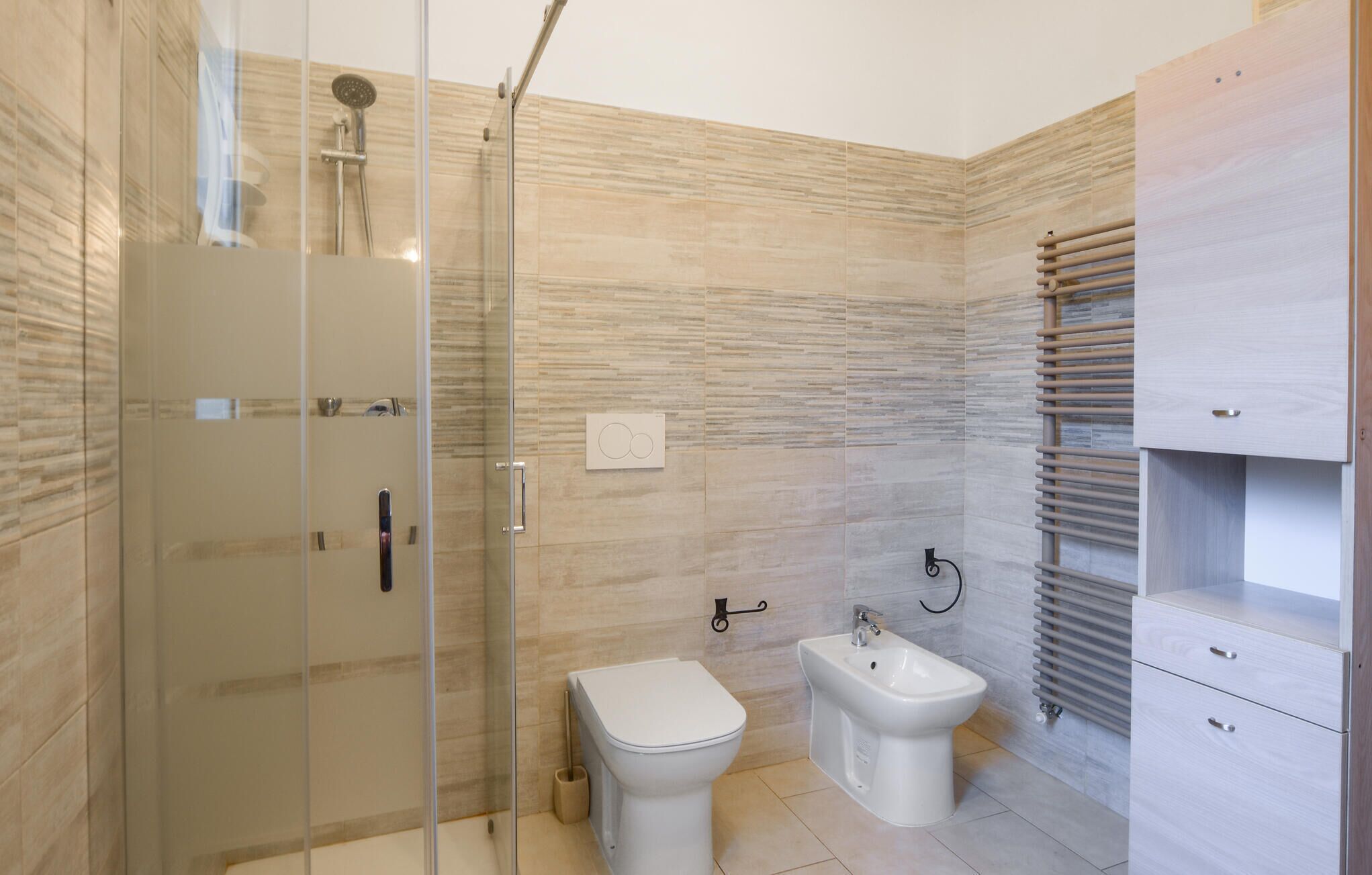 A modern bathroom with a glass shower enclosure, a toilet, a bidet, and a built-in sink.