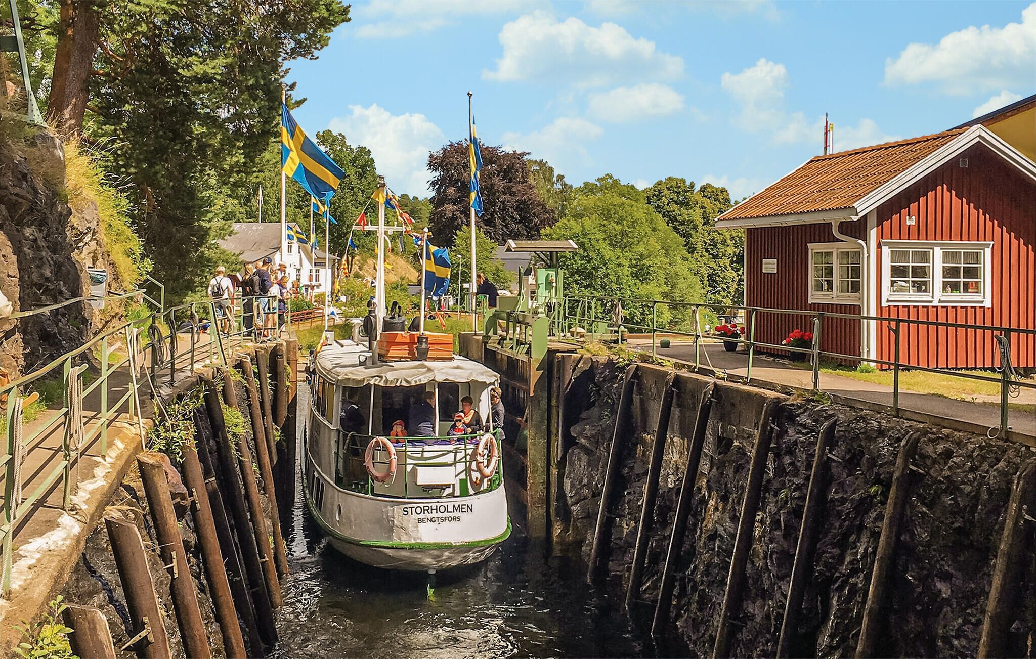 Ein Boot namens 'Storholmen' fährt durch ein Stalsystem, nebenan ein rotes Gebäude.