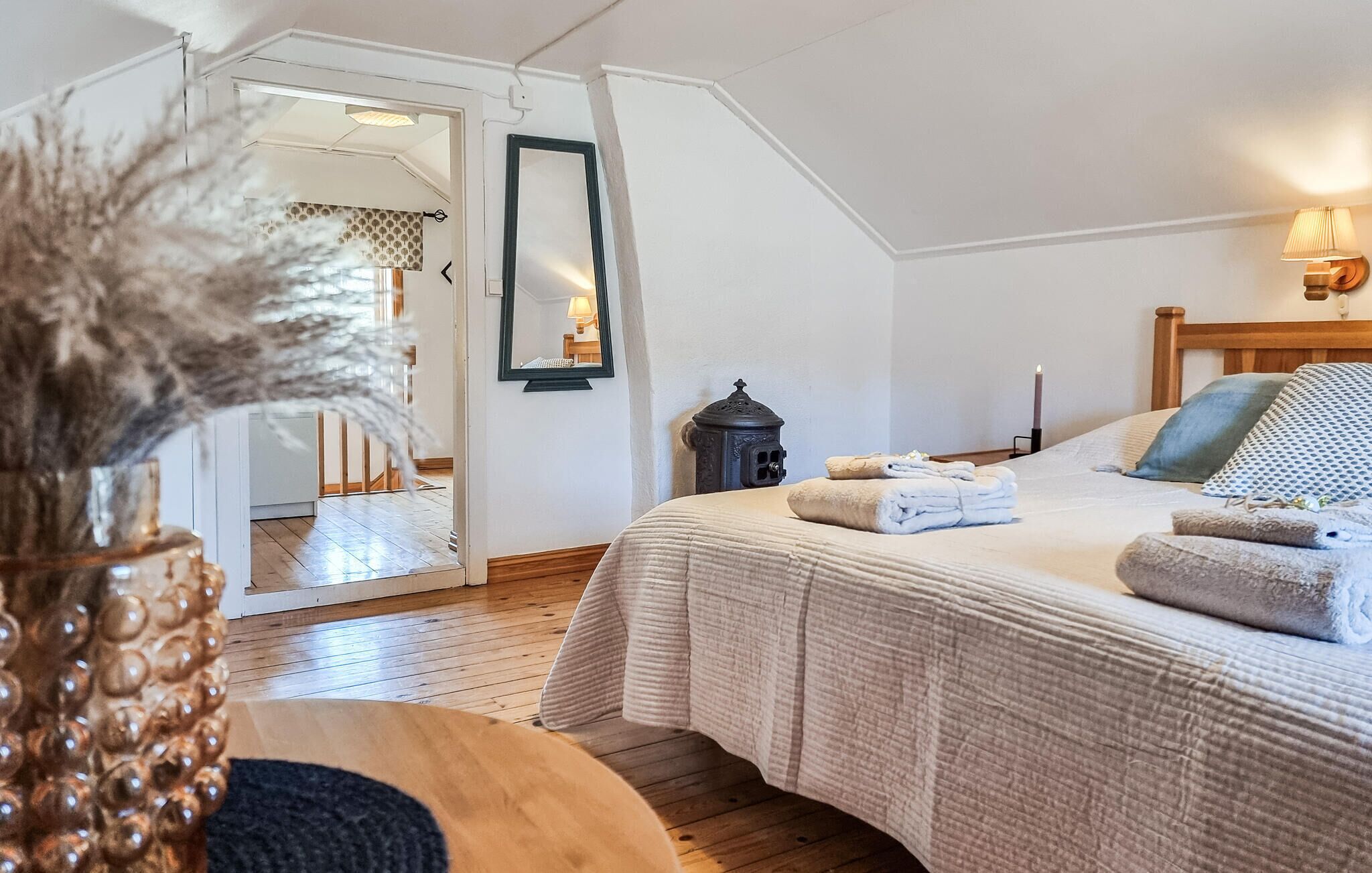 A bedroom with a bed, a nightstand, a mirror, and a lamp.