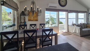 A dining area with a chandelier, a dining table, and chairs. There is a large window with a view of the water and a clock on the wall. - Pet friendly home in Mosterhamn with sauna (Mosterhamn)