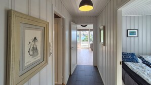 A hallway with a framed artwork on the left, a bed with patterned bedding on the right, and a view of a balcony with a table and chairs. - Pet friendly home in Mosterhamn with sauna (Mosterhamn)