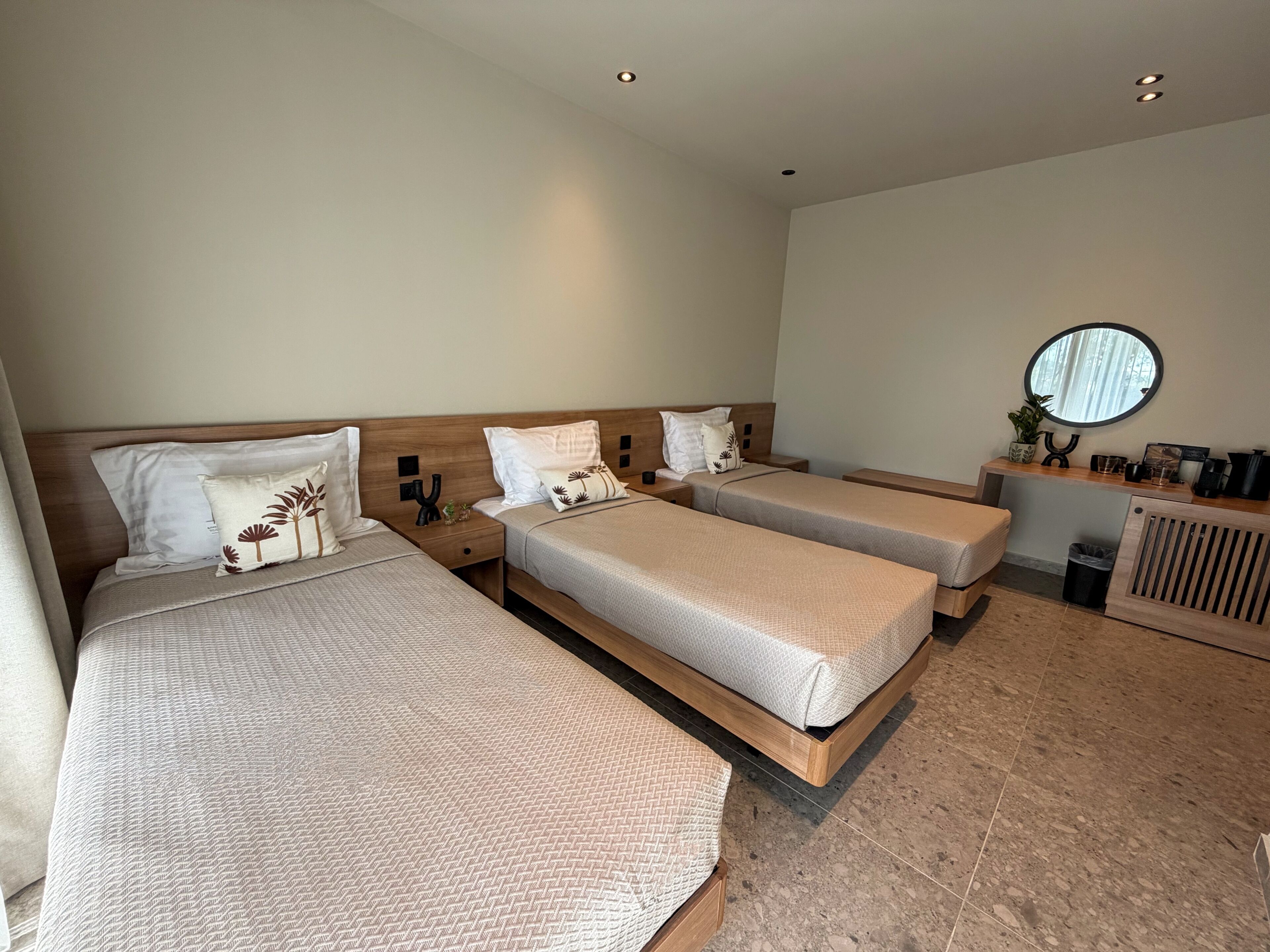 Ein Hotelzimmer mit drei Betten, einem kleinen Schreibtisch, einem Spiegel und einer Heizung.