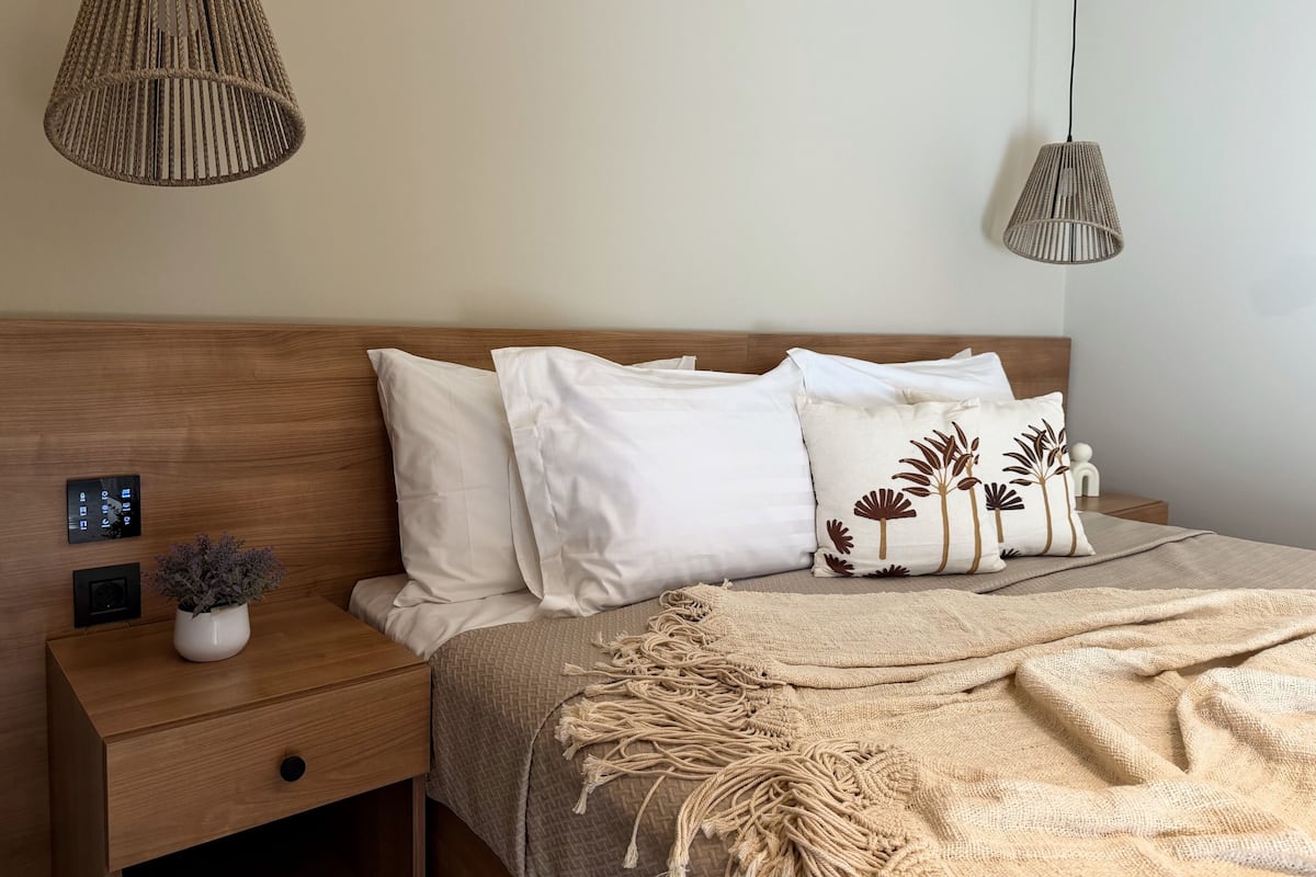 A neatly arranged bedroom with a wooden headboard, white bedding, and two hanging lamps.