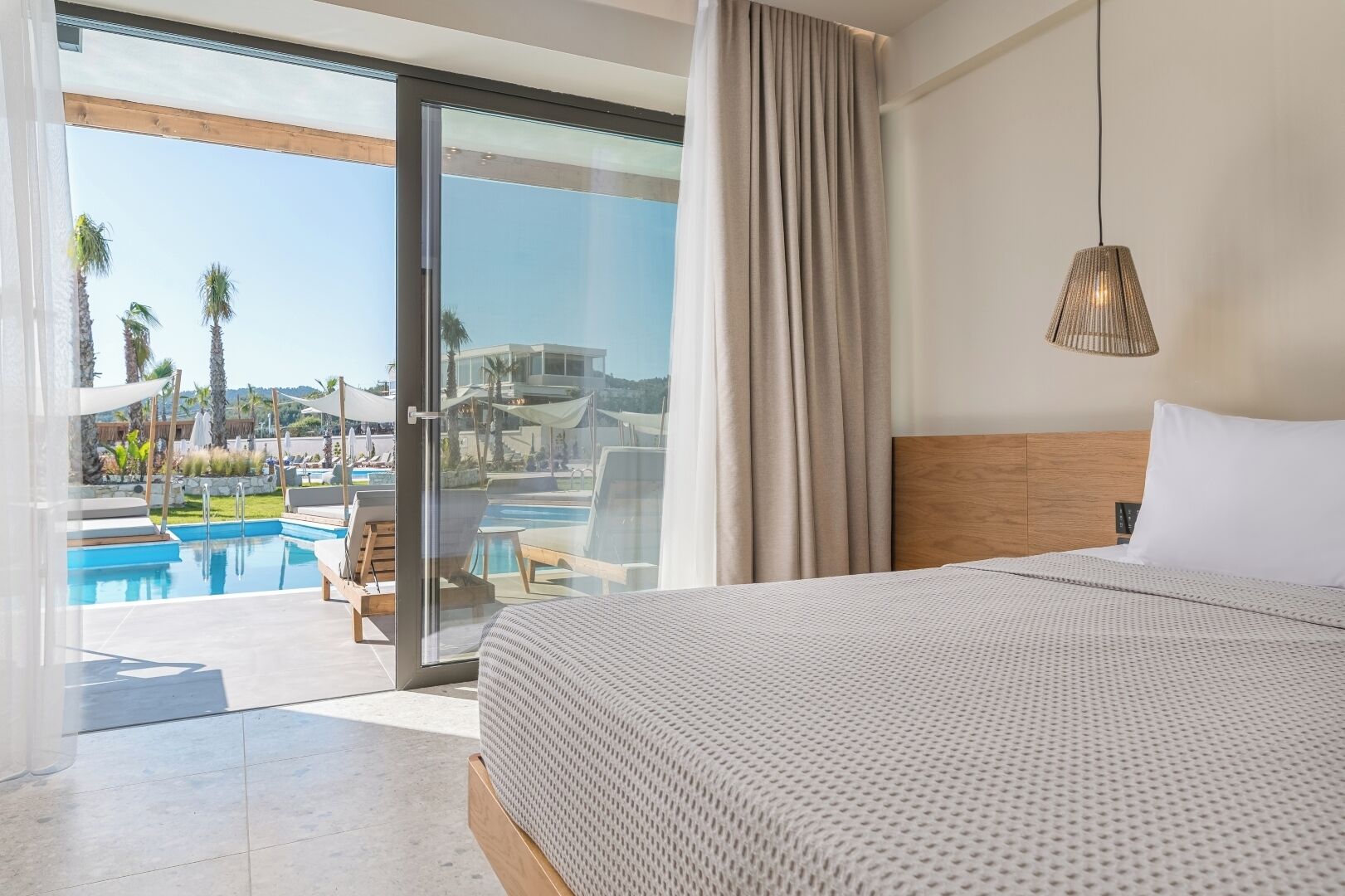 A hotel room with a large bed, a view of a swimming pool, and a glass door leading outside.