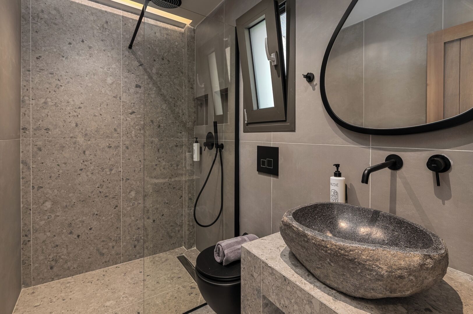 Un bagno moderno con un lavabo in pietra, un soffione a mano e uno specchio.