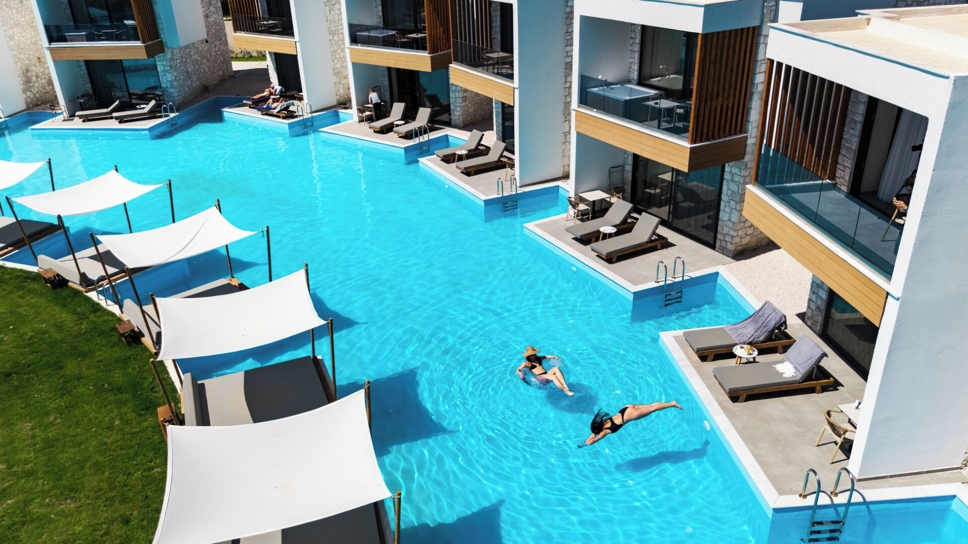 Ein Schwimmbecken mit mehreren Liegebereichen, einem Sprungturm und einer Glasbrüstung.