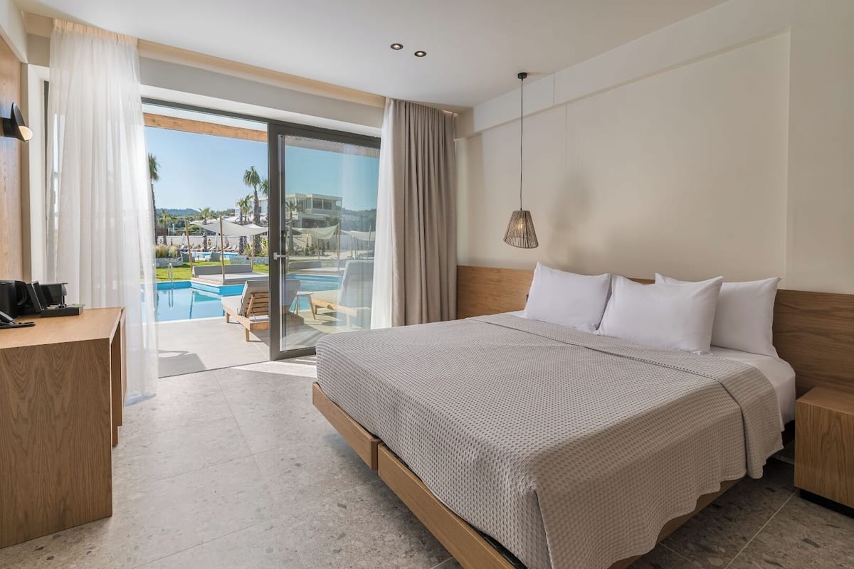 A hotel room with a large bed, a desk, and a view of a swimming pool and palm trees.