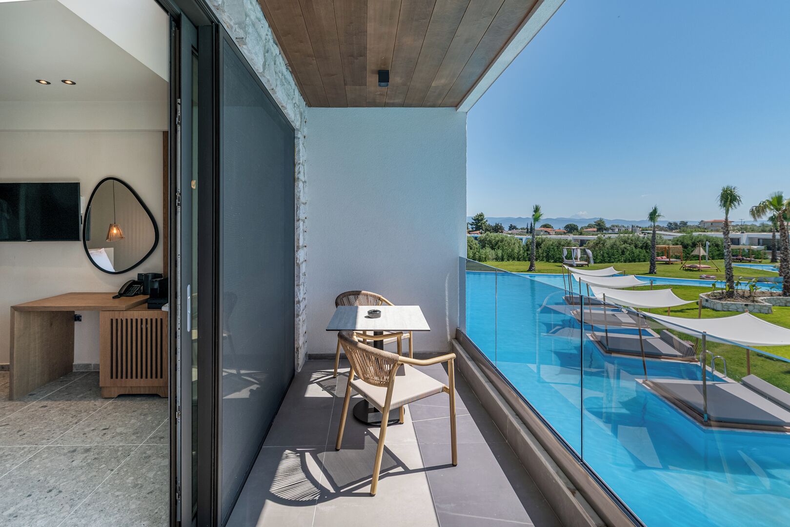 Un balcón con vista a una piscina, un escritorio de madera, una silla y una puerta de cristal.
