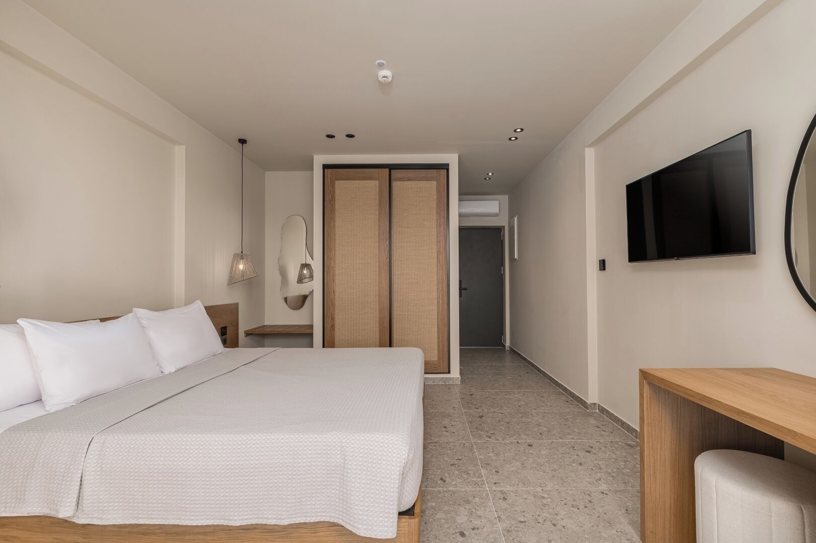Ein modernes Hotelzimmer mit einem großen Bett, einem an der Wand montierten Fernseher und einem hölzernen Schreibtisch.