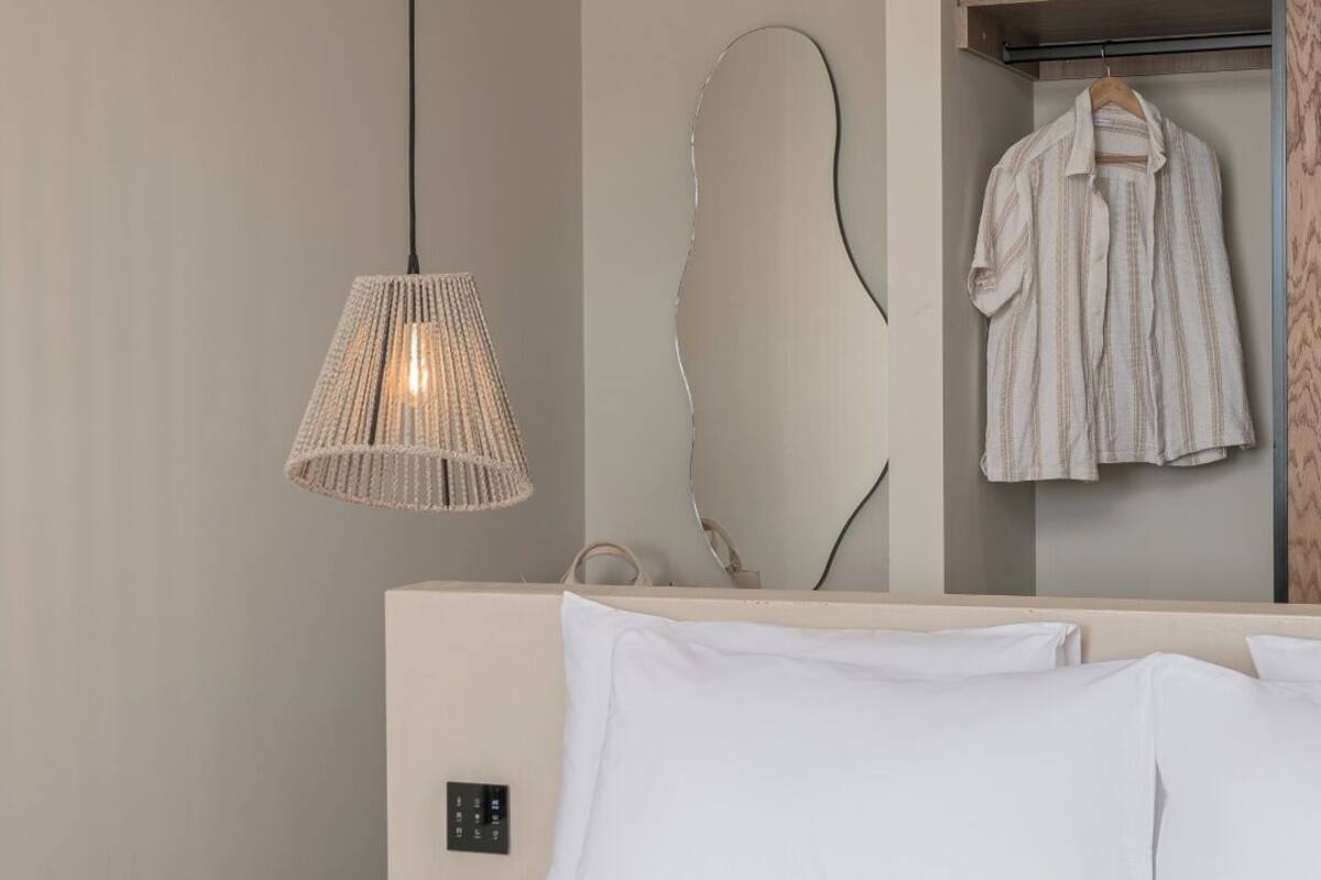 A hotel room with a bed, a hanging lamp, a mirror, and a wardrobe.