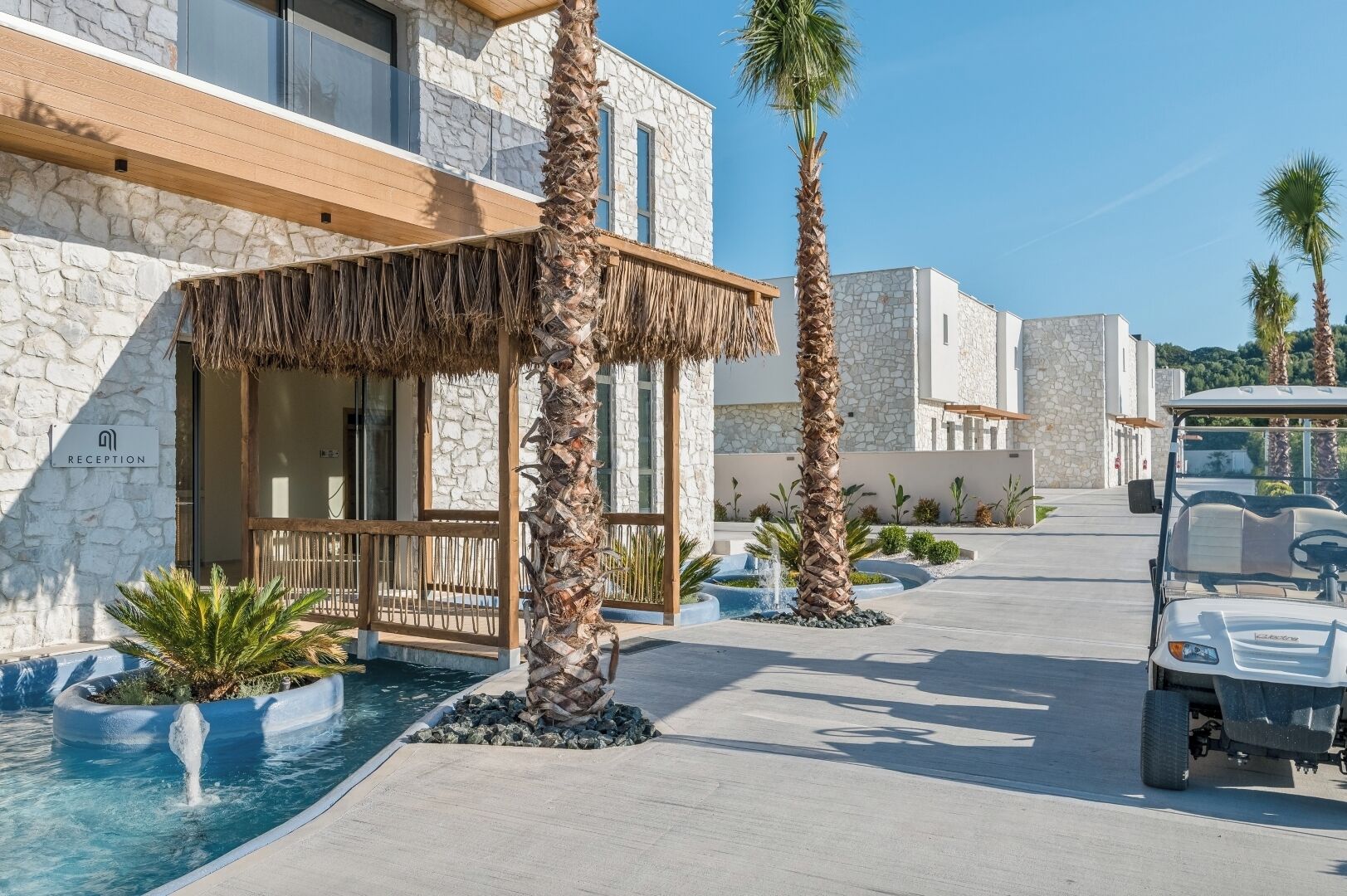 Zona de recepción con fachada de piedra, estructura de techo de paja y piscina con fuente.