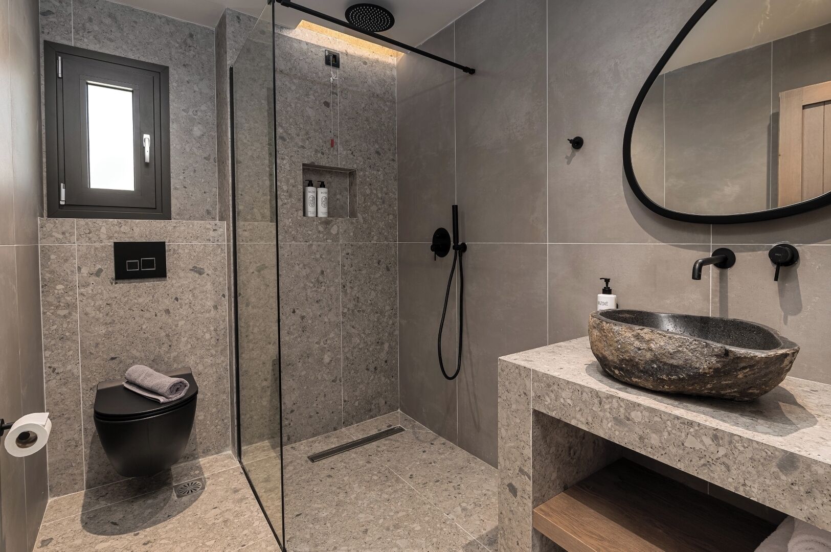 Un baño moderno con ducha envuelta en vidrio, un lavamanos grande de pedestal y un espejo.