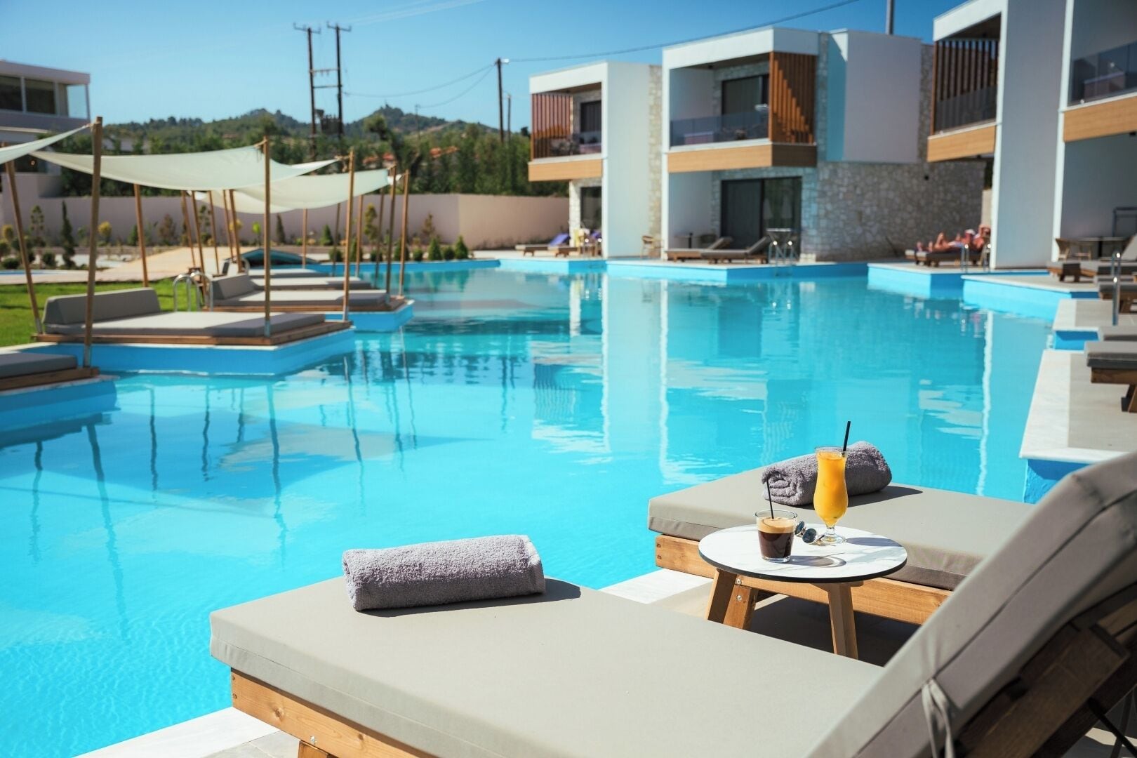 A modern pool area with lounge chairs and a table with a drink and towel.