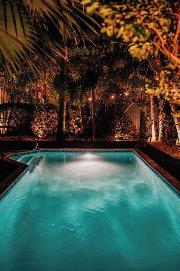 Una piscina rodeada de follaje tropical por la noche.