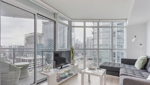 A modern living room with a large TV, a bookshelf, and a grey sofa. - 1BR Apartment in Toronto close to CN tower and Rogers Centre (Toronto)