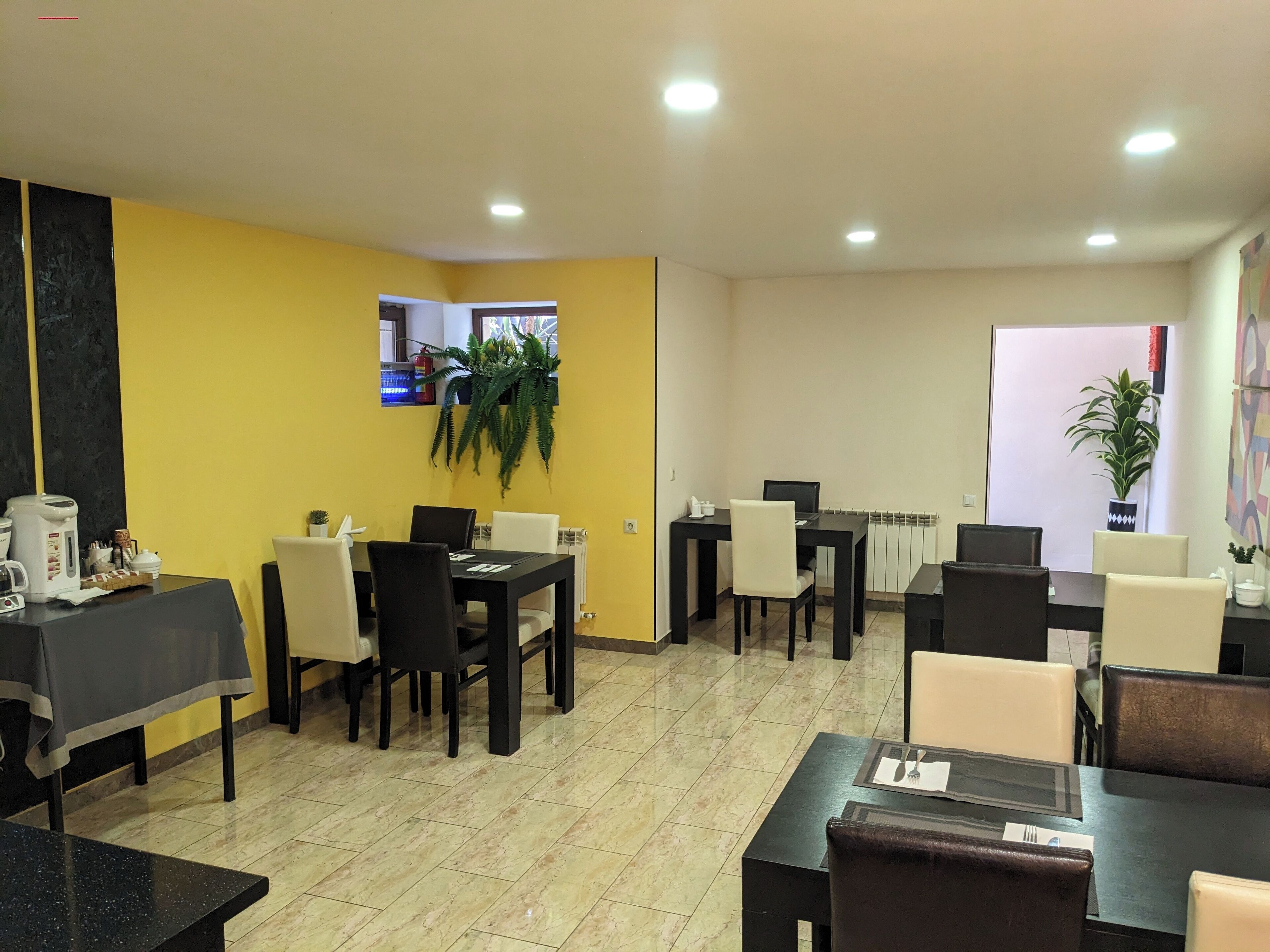 A dining area with tables and chairs, a coffee machine, and a potted plant.