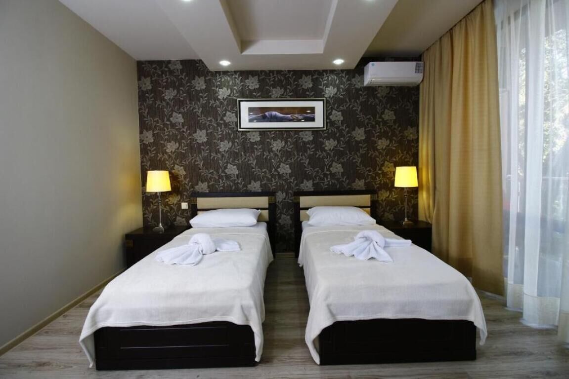Ein Hotelzimmer mit zwei Betten, floralem Wandpapier, einem gerahmten Bild an der Wand und zwei Nachttischlampen.