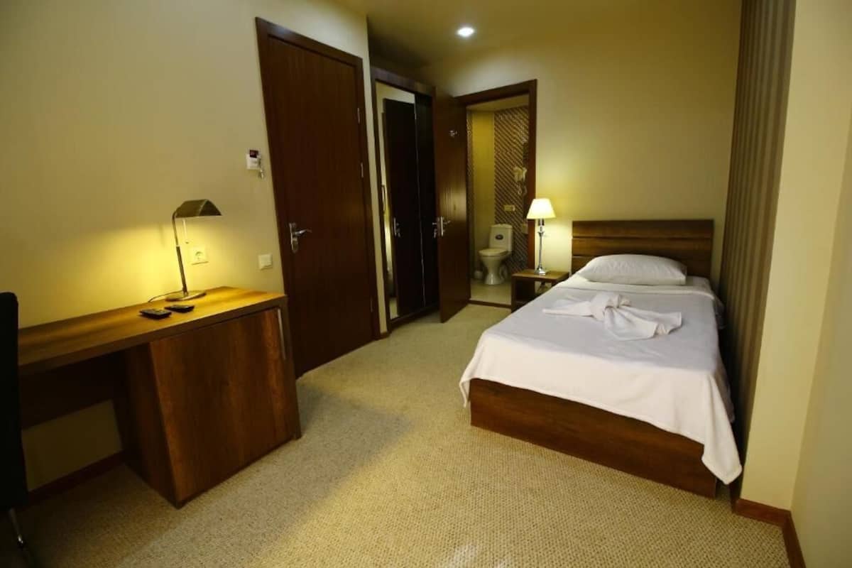 A hotel room with a bed, a desk, a chair, a lamp, and a bathroom visible through an open door.