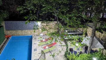 A rooftop pool area with a blue pool, lounge chairs, and a stone wall.