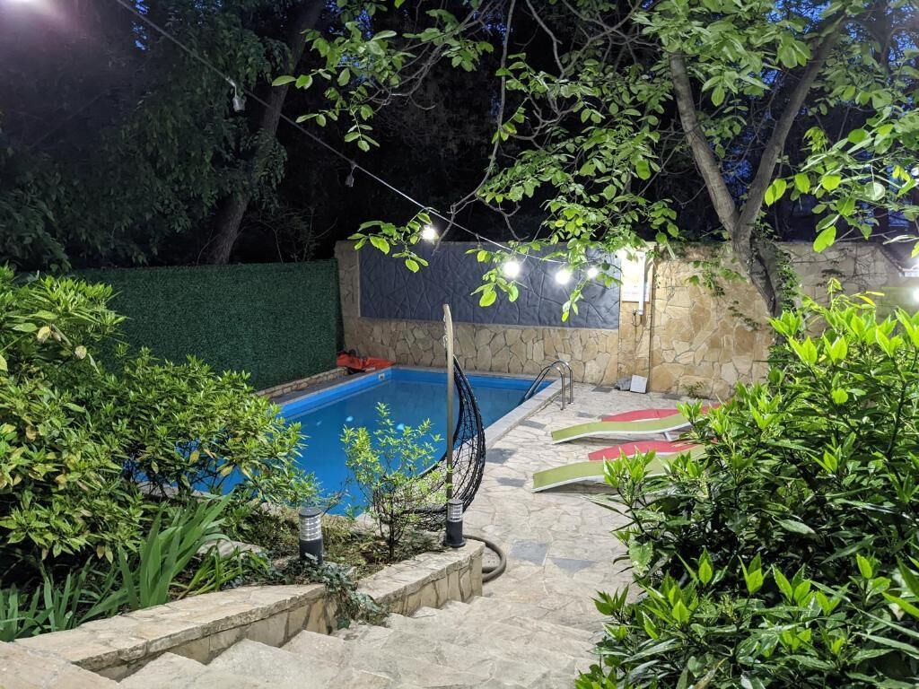 Piscina rodeada por paredes de pedra e vegetação, com luzes penduradas acima.