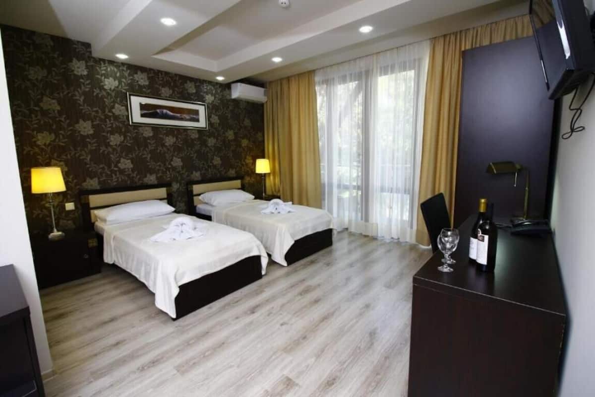 A hotel room with two beds, a desk with a bottle of wine, and a TV.