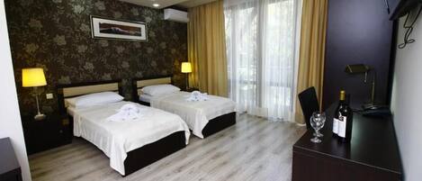 A hotel room with two beds, a desk with a bottle of wine, and a TV.