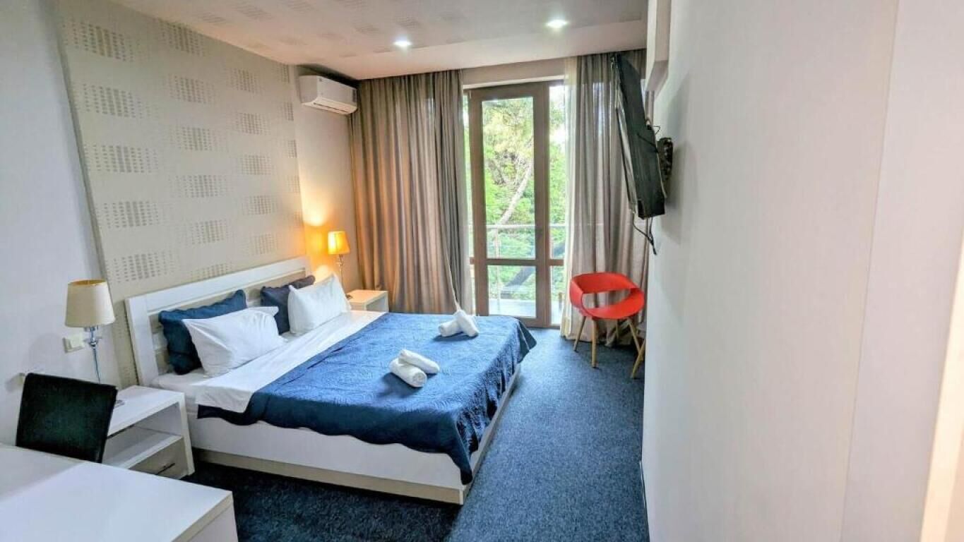Habitació d'hotel amb llit, escriptori, cadira, televisió i finestra amb cortines.