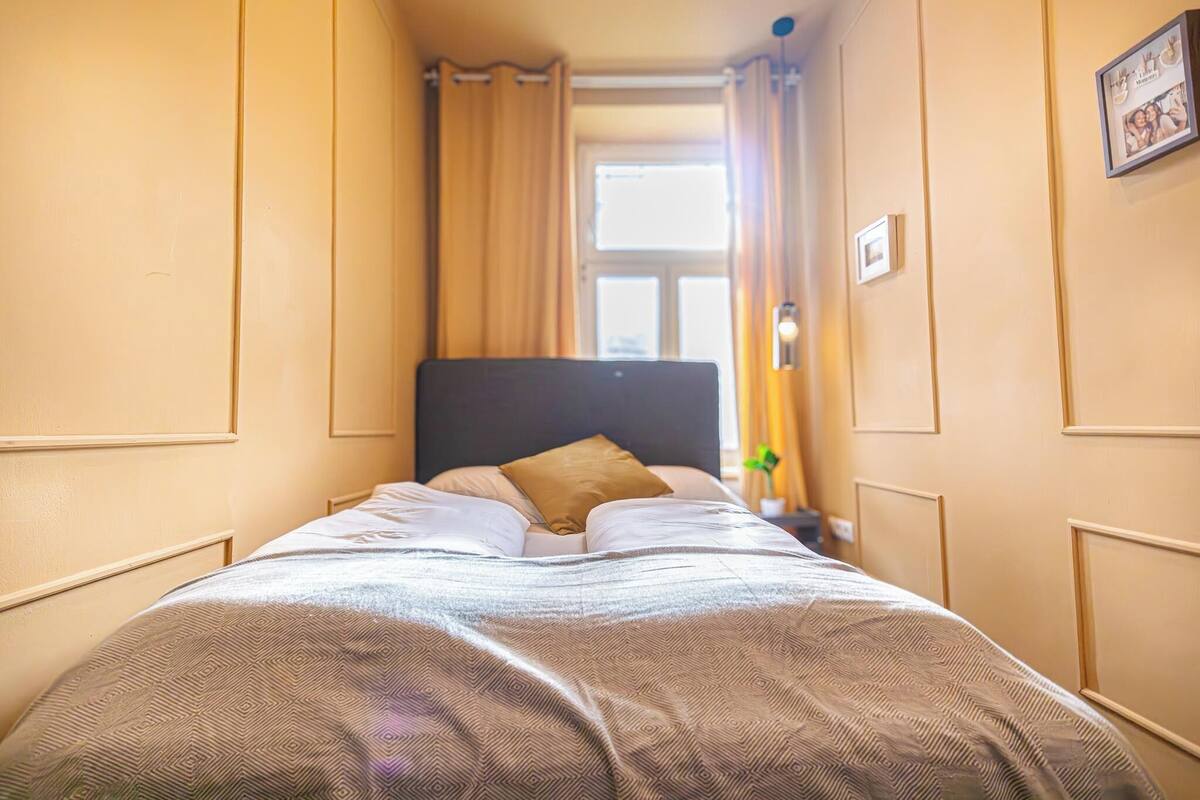 A neatly made bed with a patterned bedspread, a dark headboard, and a single brown pillow.