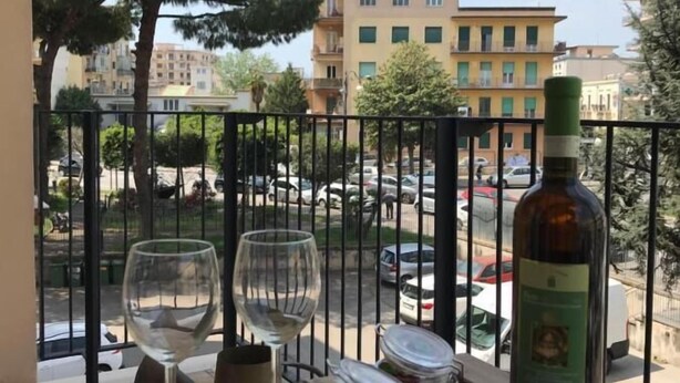 Egy erkély, ahol egy két személyre megterített asztal áll, rajta egy üveg és két fedeles üvegedény.