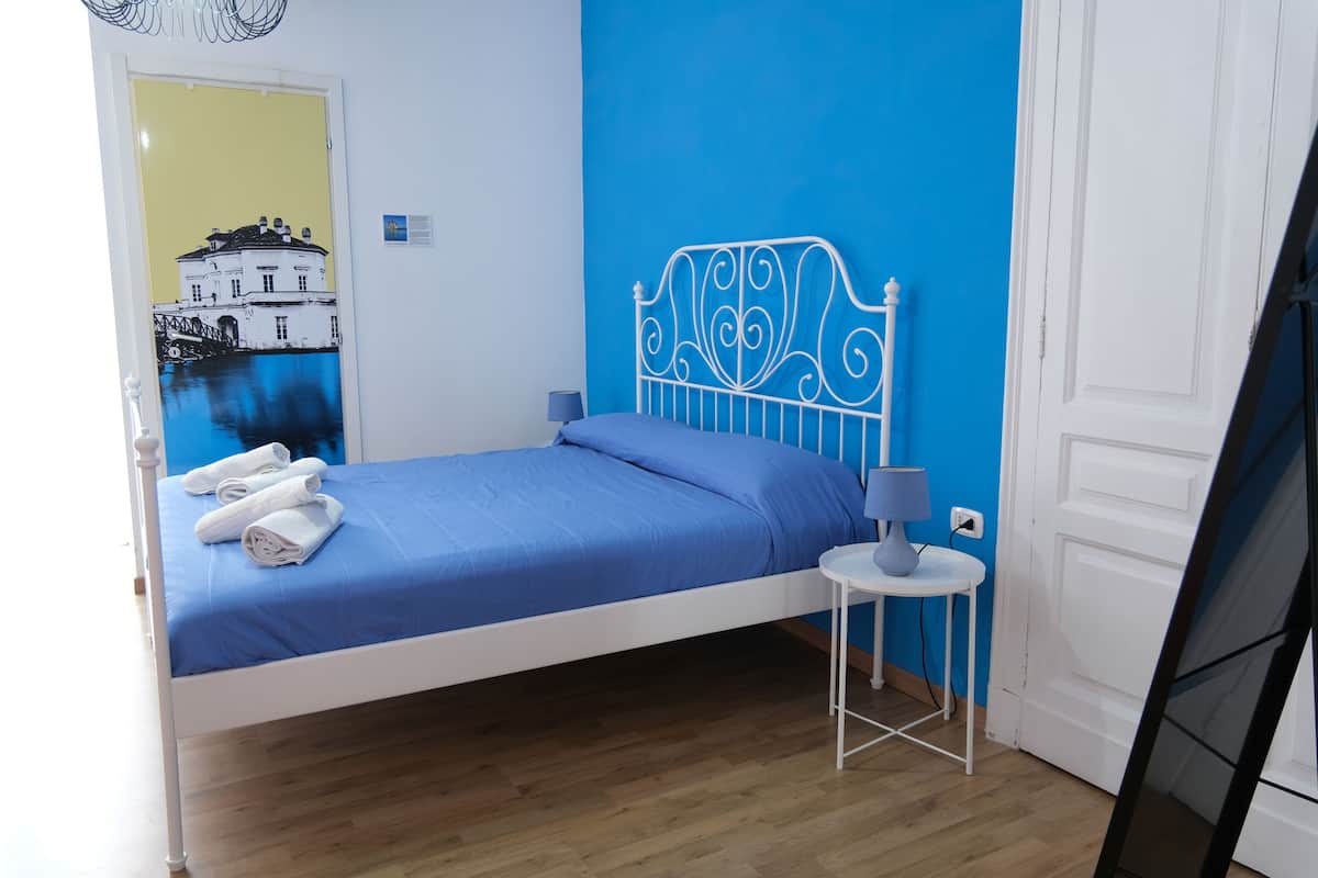 A bedroom with a bed, a side table with a lamp, and a wall with a mural.