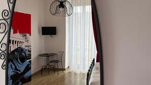 Una stanza con un letto, una televisione a muro, una sedia, un tavolo e una finestra con tende.