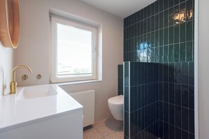 A bathroom with a white sink, a toilet, and a window. - Coastal Inn - Private Room + Balcony (Zandvoort)