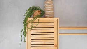 A wooden slatted cabinet with a woven basket and a tall vase with dried plants on top. - Coastal Inn - Private Room (Zandvoort)