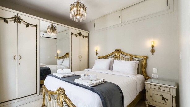 A bedroom with a large bed, a wardrobe, a nightstand, and a chandelier. - Xuru Stays I Authentic Traditions Cozy Stays, 1bdr (Cairo)