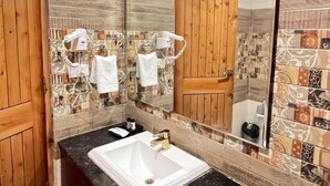 A bathroom with a wooden door, a sink with a gold faucet, and a mirror reflecting the room. - Azure Chandertal Regency Hotel And Spa (Manali)