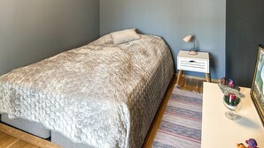 Een slaapkamer met een bed, nachtkastje, lamp en een klein tafeltje met decoratieve objecten.