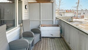 Een overdekte veranda met rieten meubels en een witte opbergkist.
