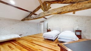 A room with two beds, wooden flooring, exposed wooden beams, and a small table with a lamp.