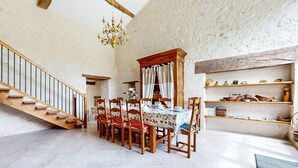 A dining area with a wooden staircase, a chandelier, and a rustic wall.