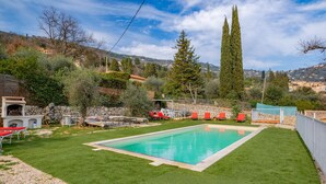 A rectangular swimming pool surrounded by a well-maintained lawn, with a stone wall and a stone staircase leading up to a house. - Beautiful home in Peymeinade (Peymeinade)